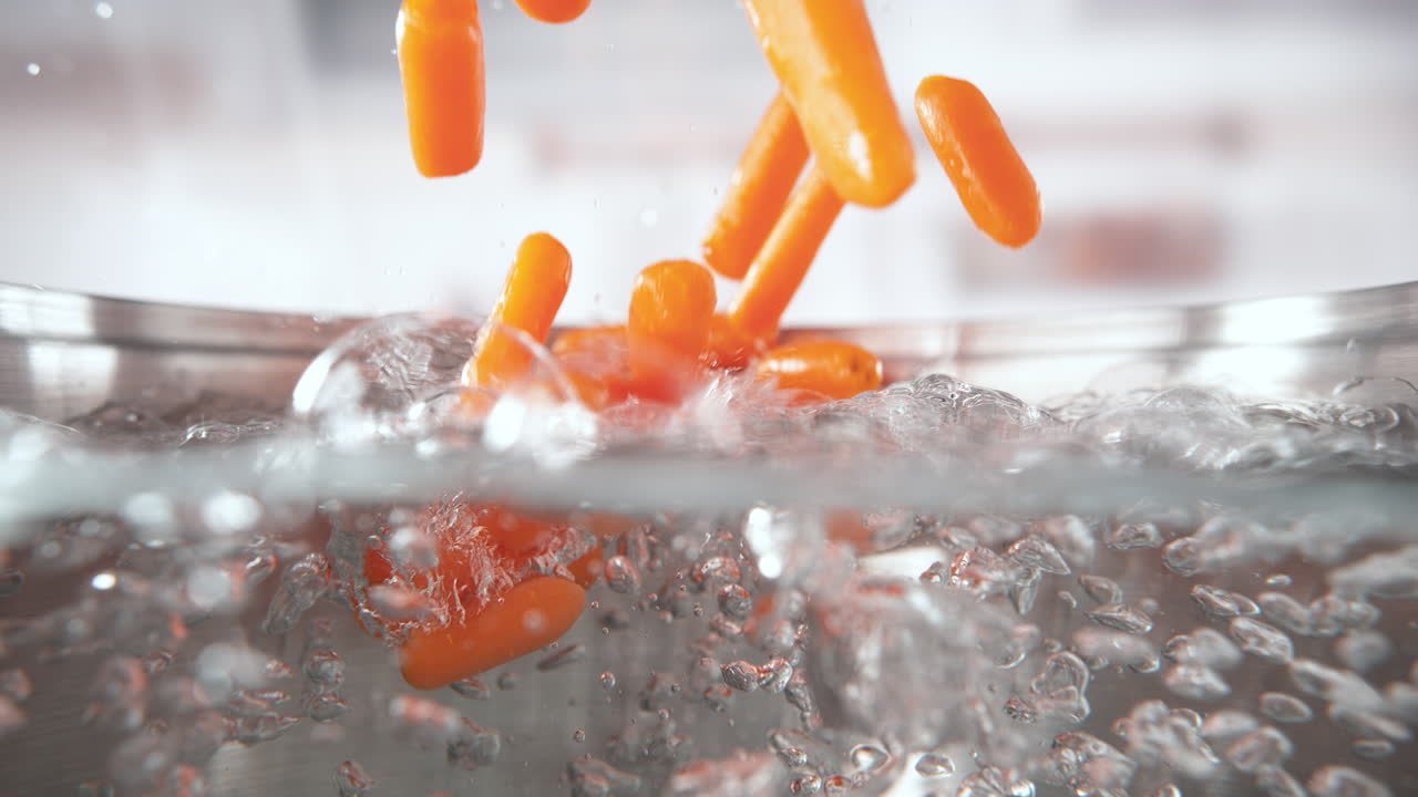 아기 당근은 는 물의 비에 떨어지고 뜨거운 액체에 침몰하여 수프, 매크로 및 느린 동작을 위해