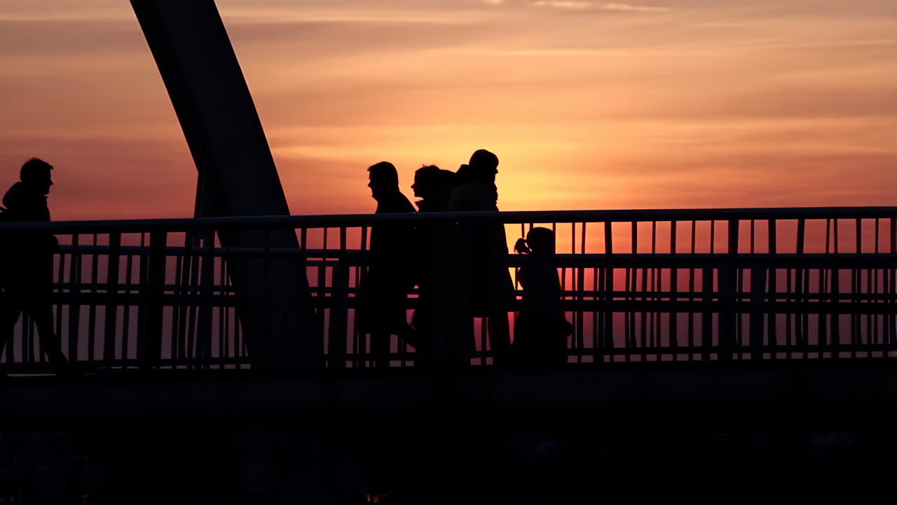 Silhouettes of people walking on a bridge at sunset