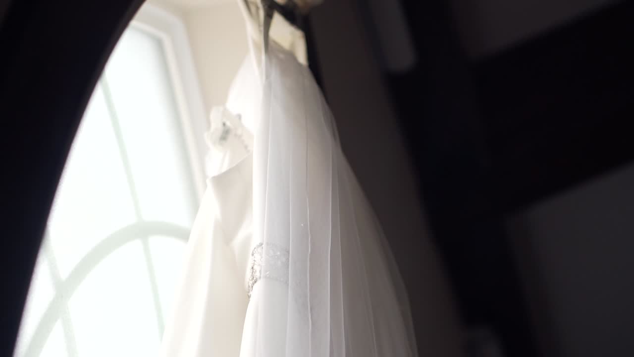 Close up side shot of a beautiful wedding dress hanging in a large window sill with a close up left to right pan