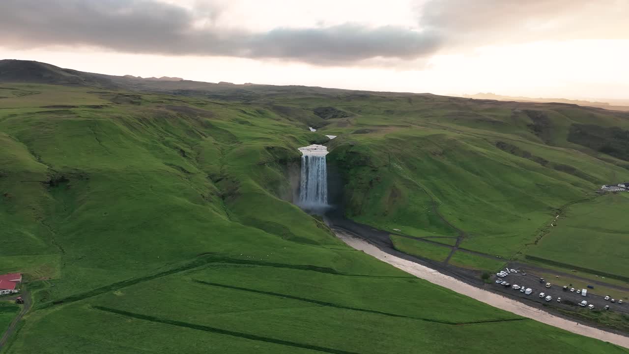 skogafoss, sur de islandia - paisaje verde y cascada descendente durante el verano - toma estática de un dron