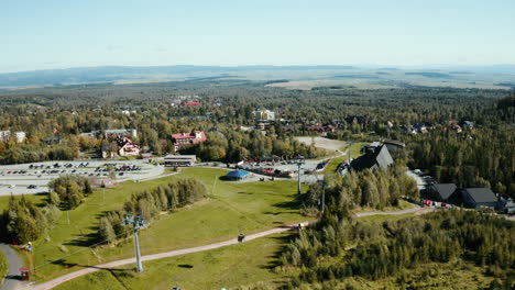 Aerial-drone-shot-getting-closer-to-a-village-below-the-water-dam-in-the-High-Tatras,-showcasing-tree-crowns-and-lush-green-summer-trees-in-Slovakia,-Europe