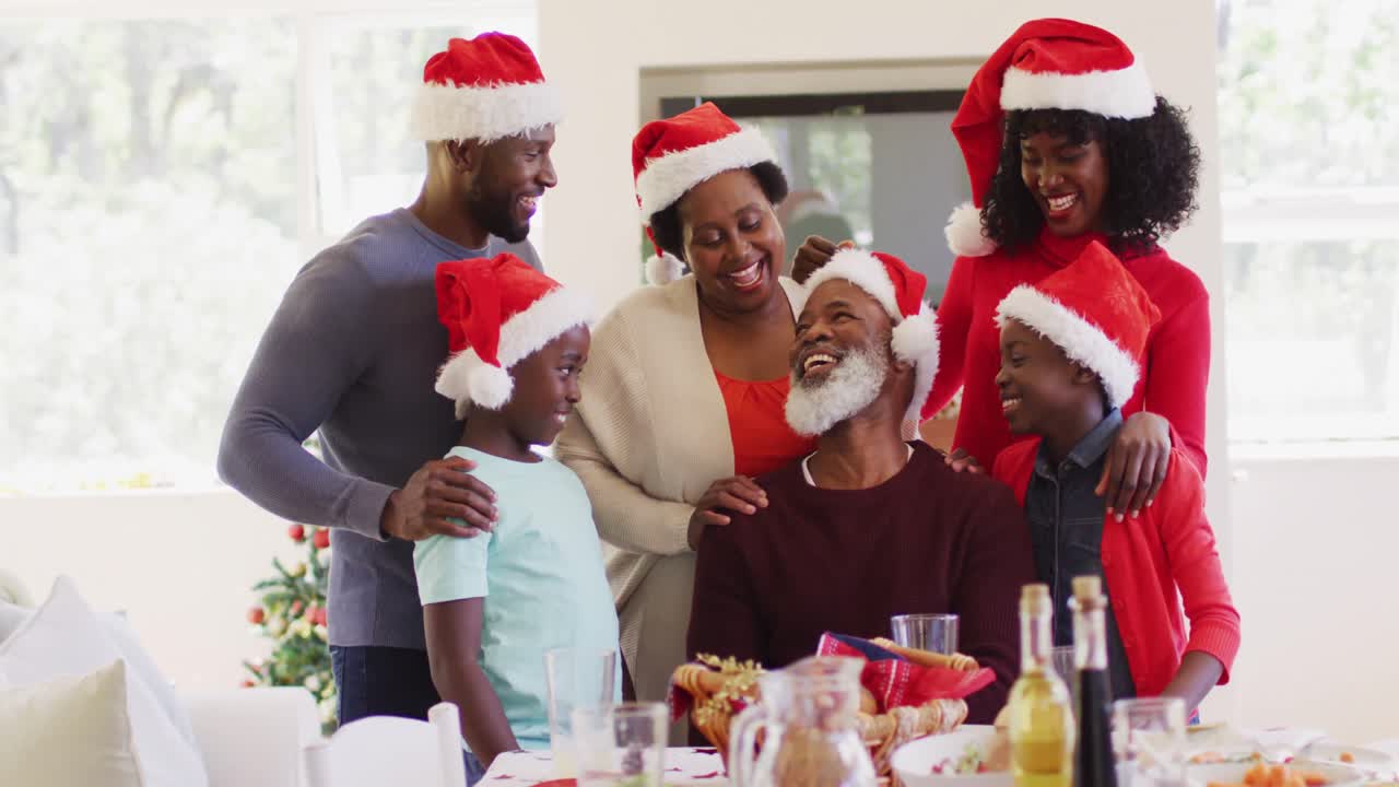 Noel şapkalı Afro-Amerikalı bir aile, evde birlikte sohbet edip gülümsüyor.
