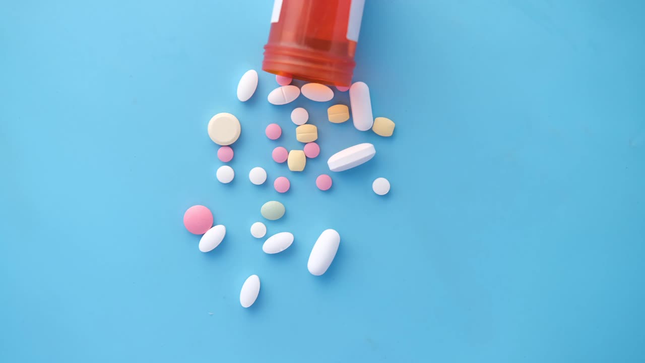 Assorted pills and capsules spilling from an orange bottle