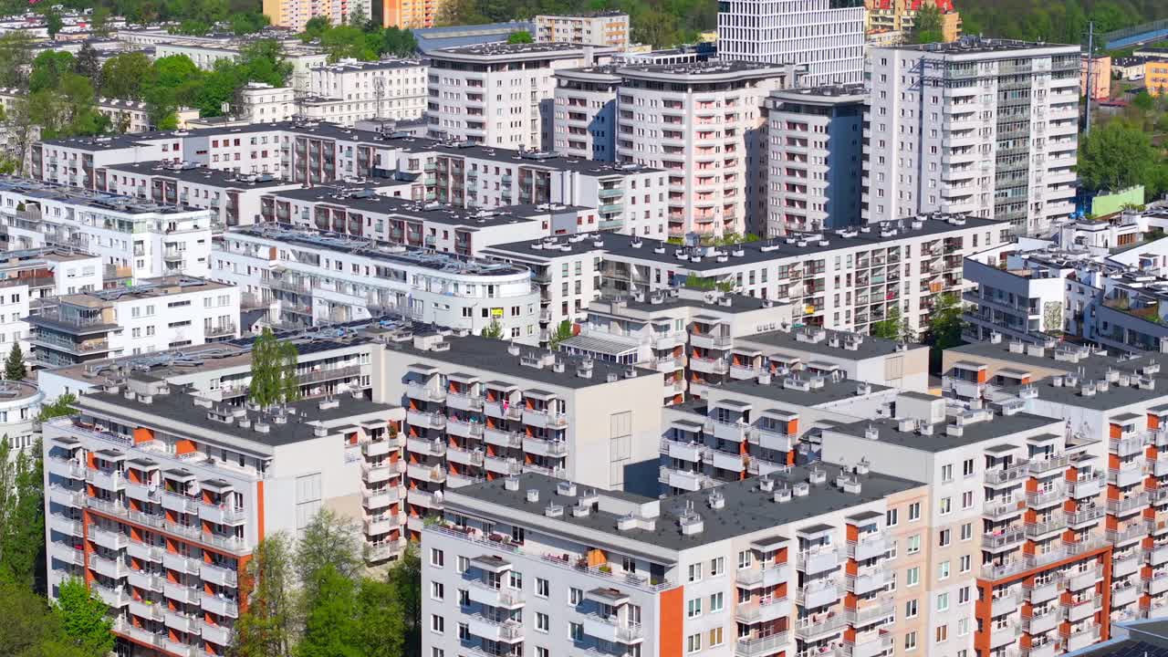 Drone aerial view of residential apartment blocks in Warsaw’s Wola district, showcasing dense housing, balconies, and urban greenery under bright spring sunlight