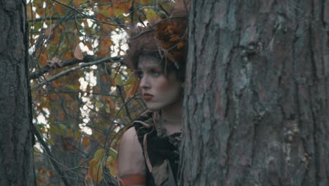 beautiful woman hides on a tree trunk in forest at daytime