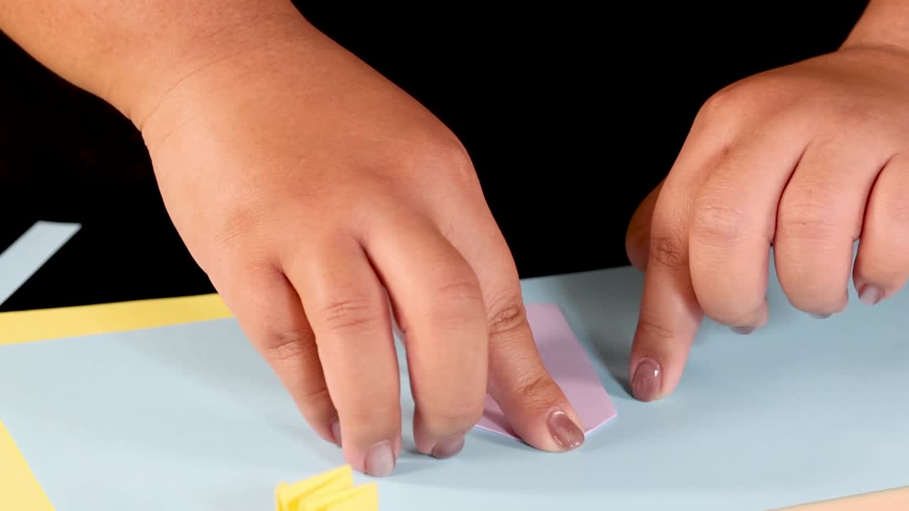 Close-up of hands carefully folding a pink paper strip against a light blue background