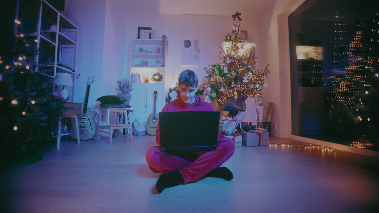 hombre feliz usando una computadora portátil mientras está sentado en el suelo en casa durante la navidad