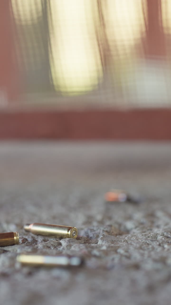 Primo piano verticale di bossoli vuoti che cadono e rimbalzano su un pavimento di cemento di un poligono di tiro.