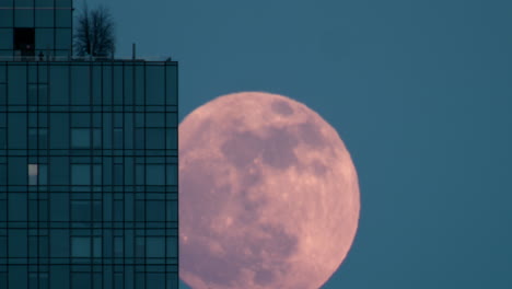 pink full moon emerging from behind new york city skyscraper with blue sky