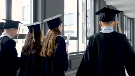 kindergarten students in cap and gown holding graduation diploma and walking in the school corridor