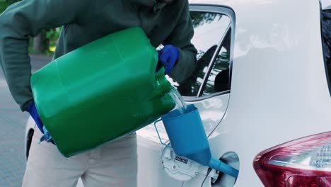 a man pouring gasoline into an empty fuel tank from a plastic red  gas can. filling  the car from the canister into the neck of the fuel tank.