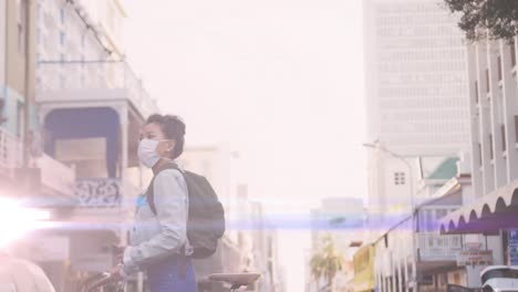 animation of light spots over biracial woman with face mask walking with bicycle