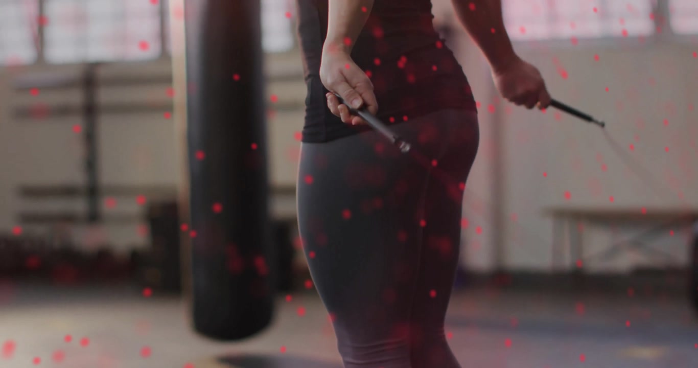 Female fitness enthusiast rotating wrists and jumping rope near punching bag for building endurance
