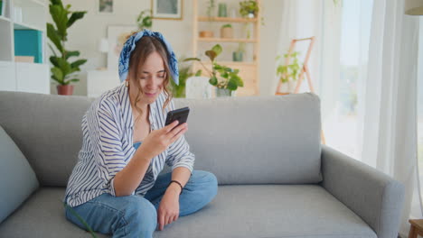 Mujer-Sonriente-Disfrutando-Del-Teléfono-Inteligente-En-El-Sofá-De-La-Sala