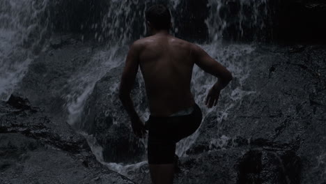 young man climbing on stone under waterfall.