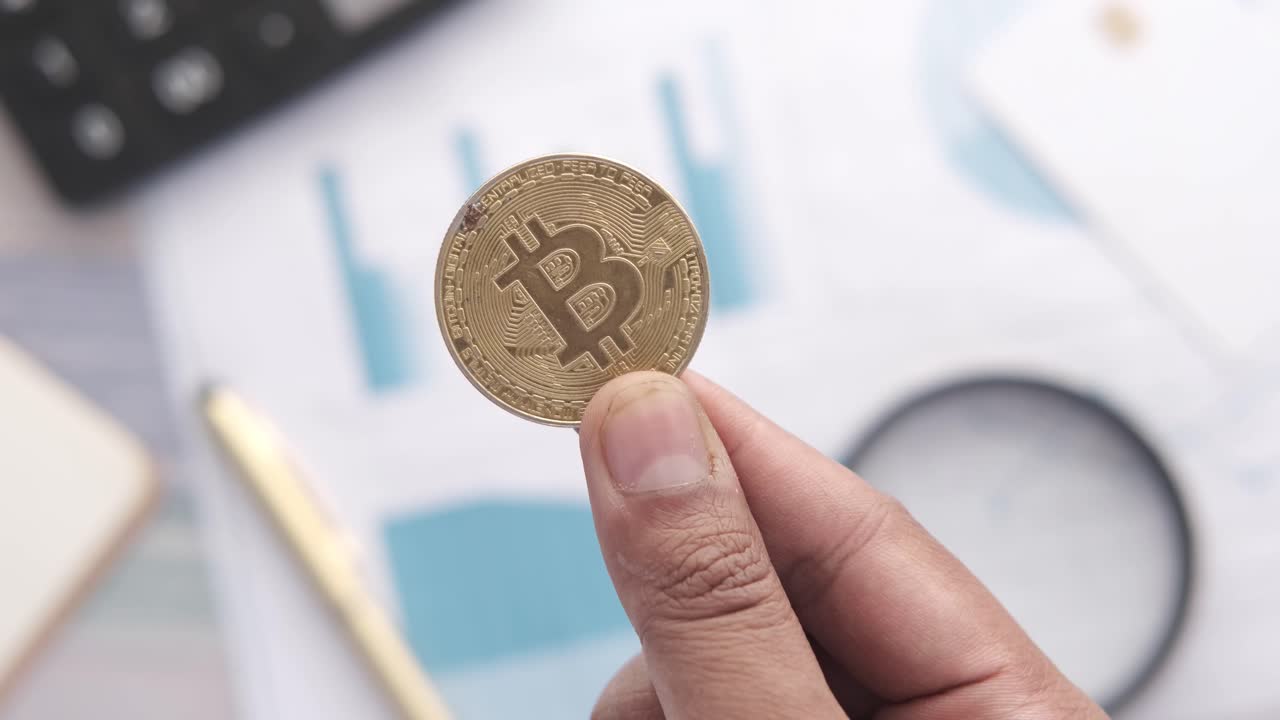 moneda de bitcoin en la mano con documentos comerciales y calculadora en el fondo