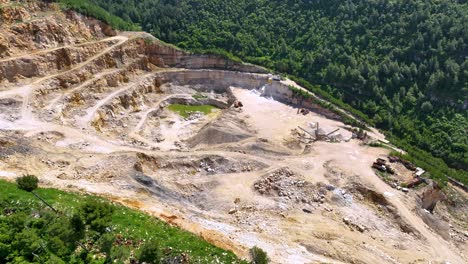 large quarry stone mining on the side of the mountain surrounded by forest and vegetation