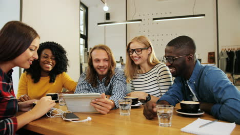 grupo multiétnico de amigos viendo un video gracioso en una tableta en un café