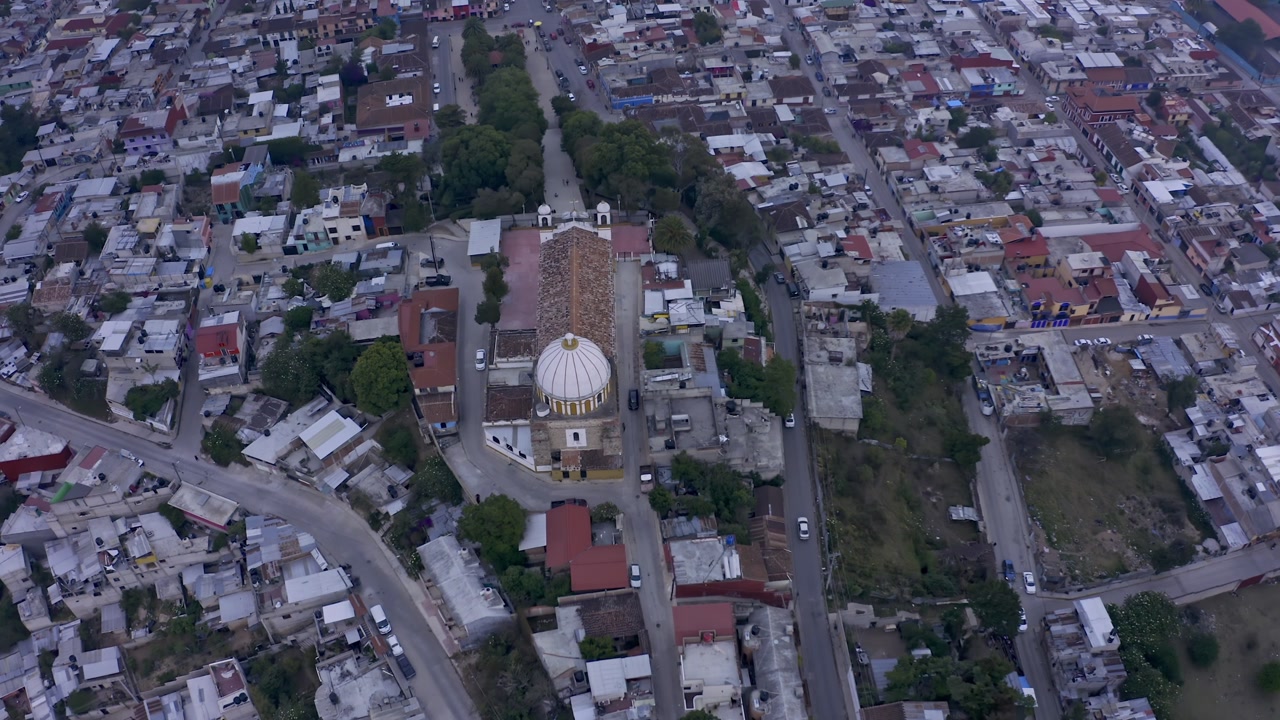 An aerial drone shot captures the charming colonial city of San Cristóbal de las Casas in Chiapas, Mexico, at sunset.