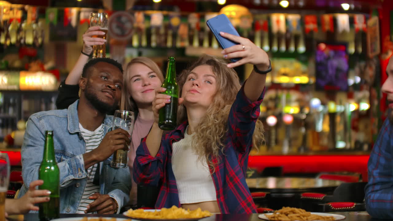 Friends are taking selfie with smartphone in bar. Young people are posing laughing and talking. Beer bottles and. Friends are taking selfie with smartphone in