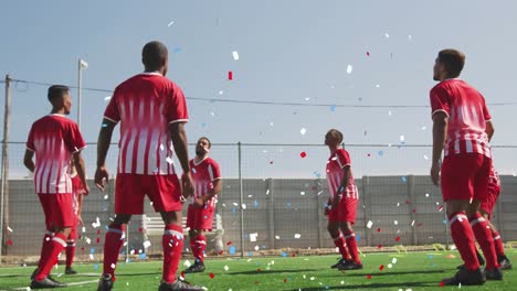 colorful confetti falling against team of male soccer players practicing on on grass field