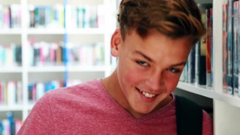 un escolar sonriente de pie en la biblioteca