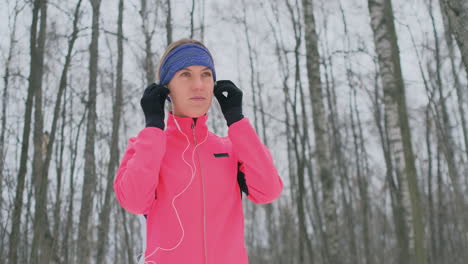 the woman before the morning winter jog inserts headphones in the ears and is preparing to run through the natural park in slow motion. listening to music while running. learn foreign languages