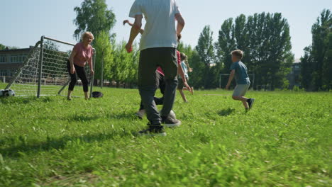 la familia disfruta de un juego de fútbol al aire libre en un día soleado mientras el hijo vestido de blanco dribla la pelota, sólo para que su hermano se deslice y patee la pelota en un momento lúdico en el campo cubierto de hierba.