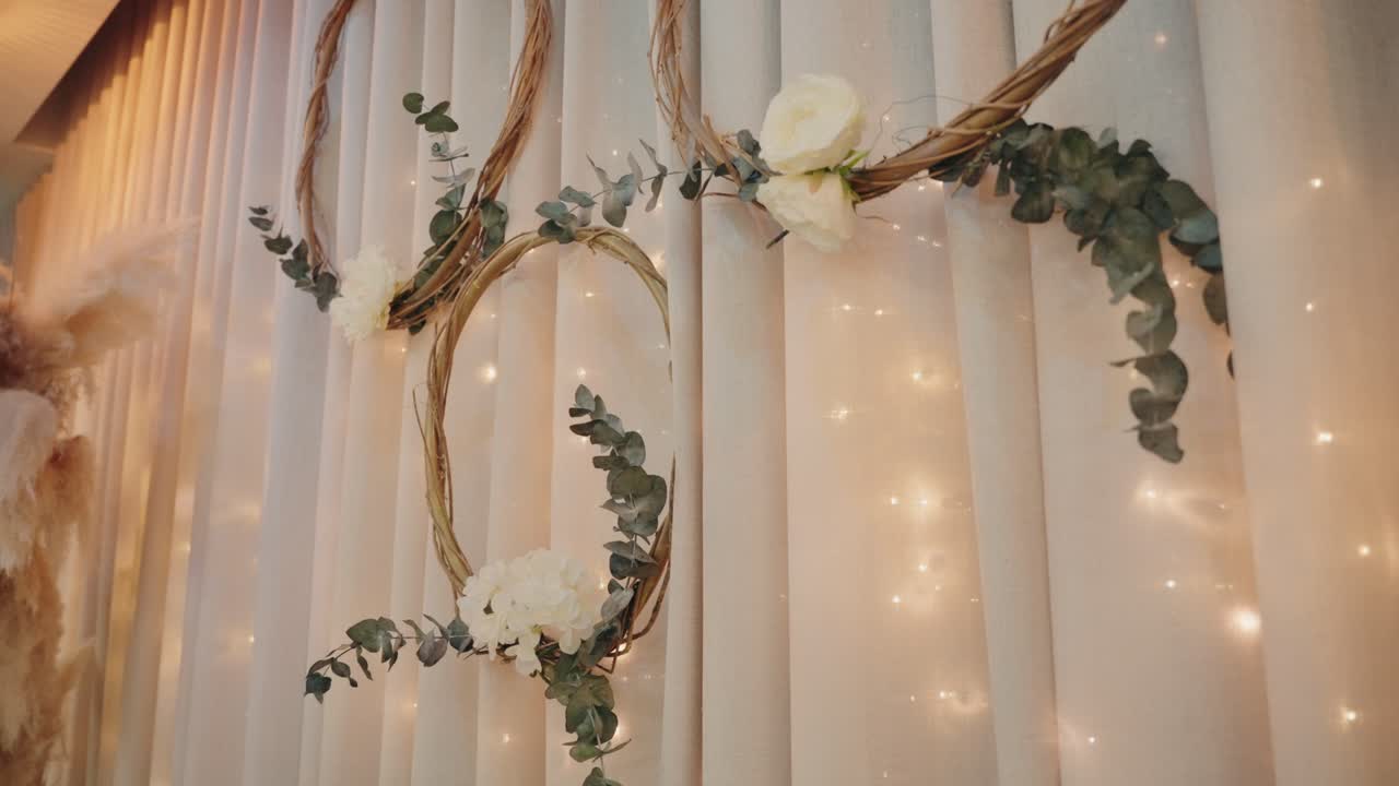 wedding floral wreaths with eucalyptus and roses hang on curtain with warm fairy lights