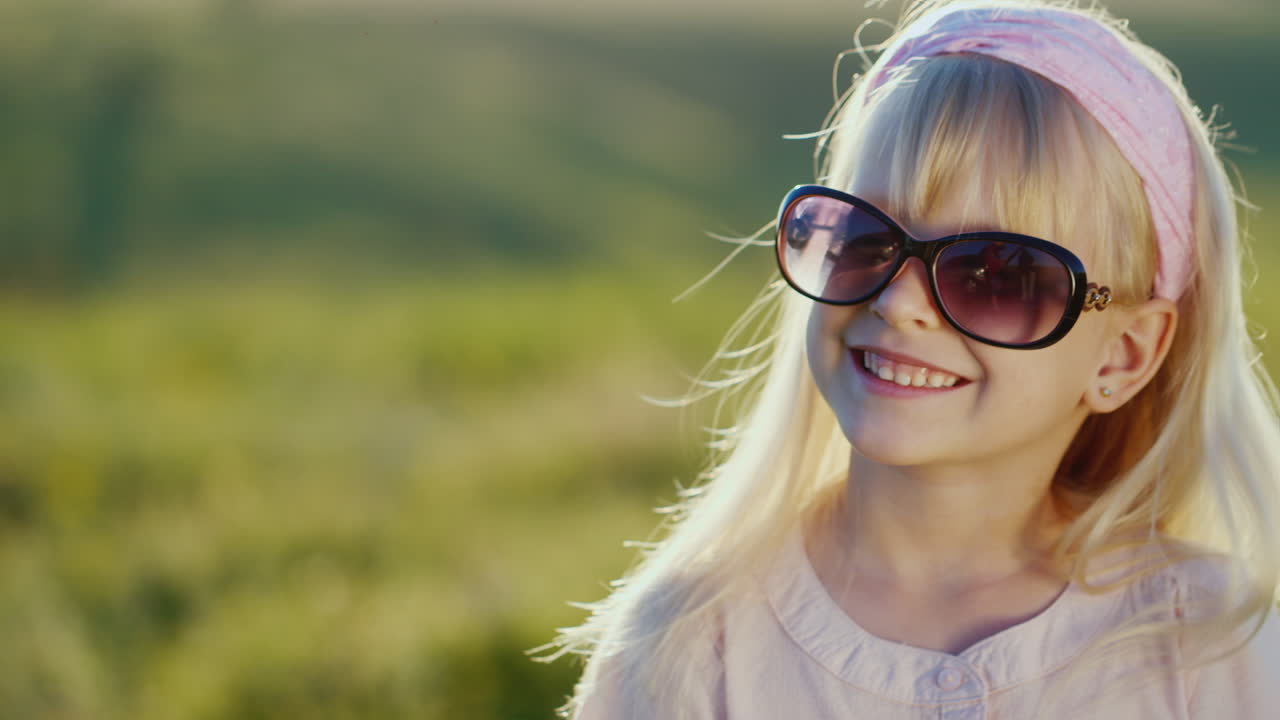 선글라스를 쓴 재미있는 금발 소녀가 카메라를 보며 웃고 있습니다.