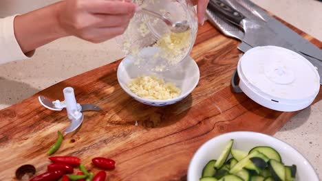 a person uses a manual chopper to prepare garlic in a kitchen, with fresh ingredients on a wooden board