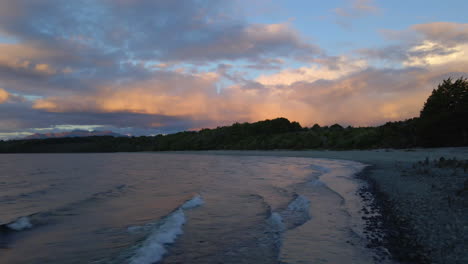 Dolly-Out-Vista-De-Olas-Rápidas-Rompiendo-En-La-Playa-Rocosa-Del-Lago-Te-Anau-En-Nueva-Zelanda-Después-De-La-Hermosa-Puesta-De-Sol