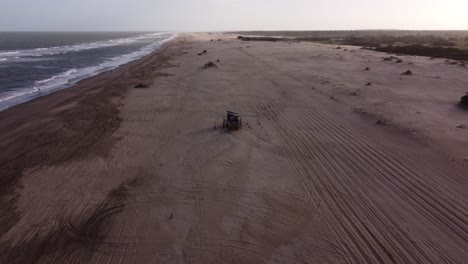 siguiente toma aérea del camión de cuatro ruedas en la playa de arena, conduciendo por un camino forestal rural al lado de las olas de agua de la playa en américa del sur, argentina