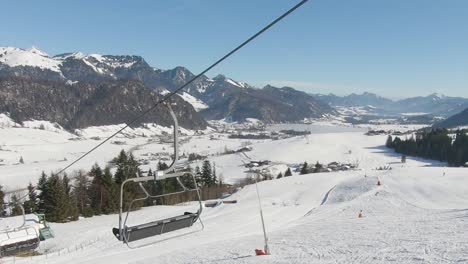 Panoramic-shot-taken-from-a-ski-lift-moving-uphill-with-skiers,-in-the-background-a-panorama-of-a-snowy-valley-and-mountain-peaks