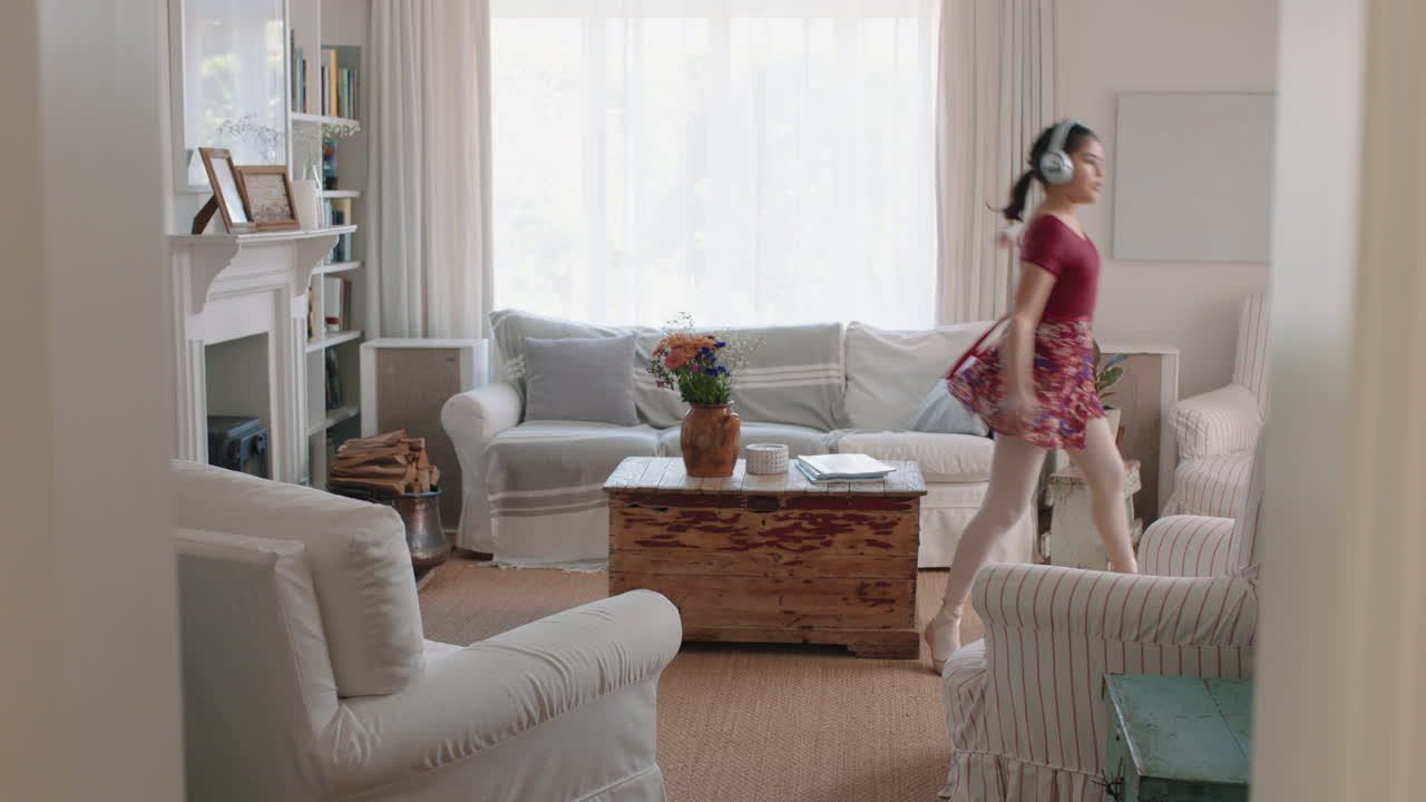 행복한 십대 소녀가 춤을 추고 집에서 발레 춤 동작을 연습하고 음악을 듣고 헤드폰을 착용하고 재미있게 주말을 즐기고 있습니다.