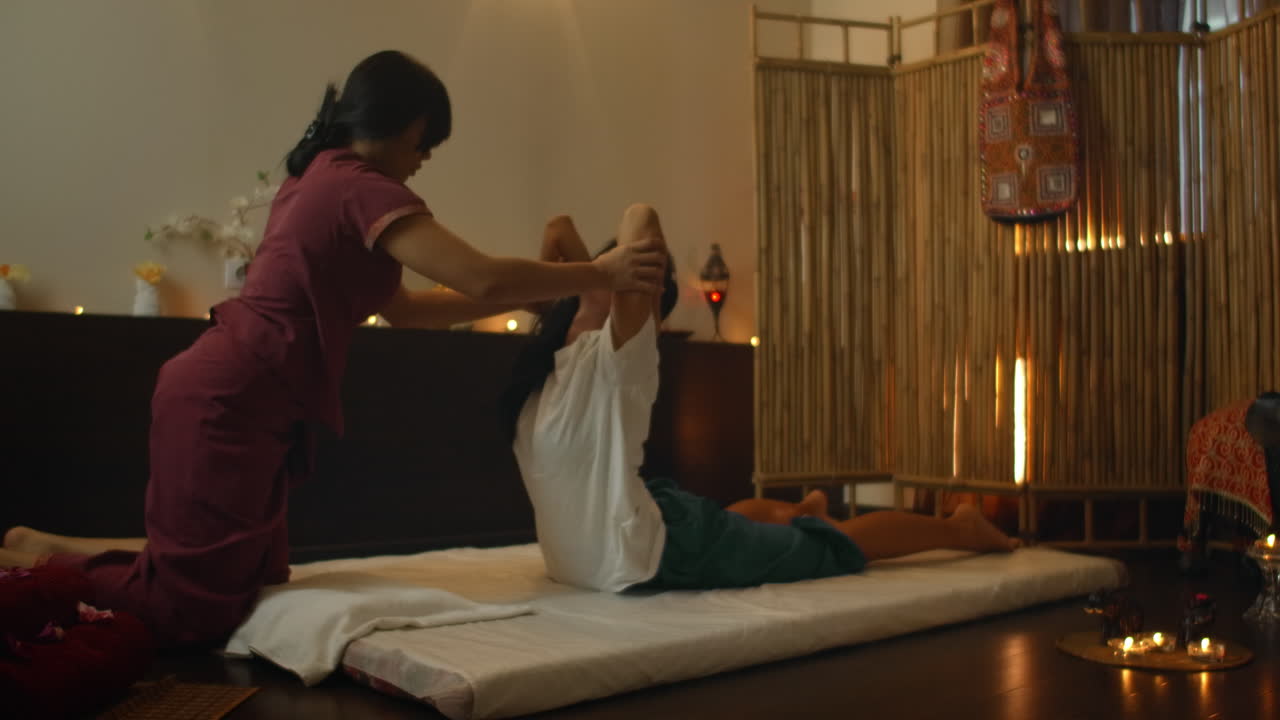 Alternative Chinese medicine an Asian woman performs therapeutic massage on the back and legs of a Caucasian woman lying on a couch. Aromatherapy and manual therapy by Chinese masters.
