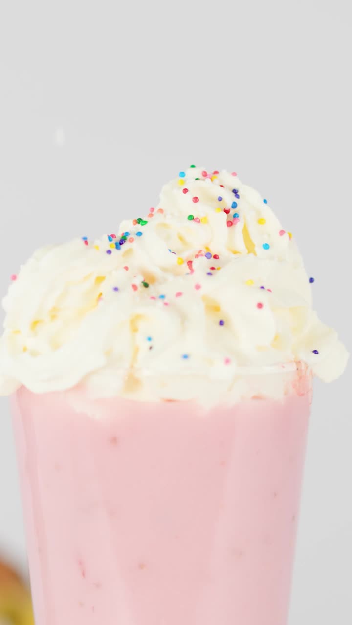 Primo piano di codette colorate che cadono sulla panna montata sopra un cremoso frullato di frutta rosa