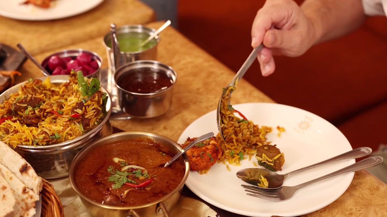 Nærbillede af en hånd, der bruger en ske til at servere krydret biryani på en tallerken.
