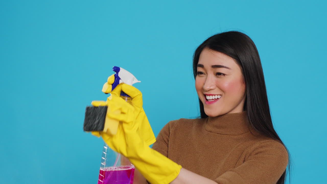Housekeeper wearing yellow rubber gloves while holding spray and duster during houseclean