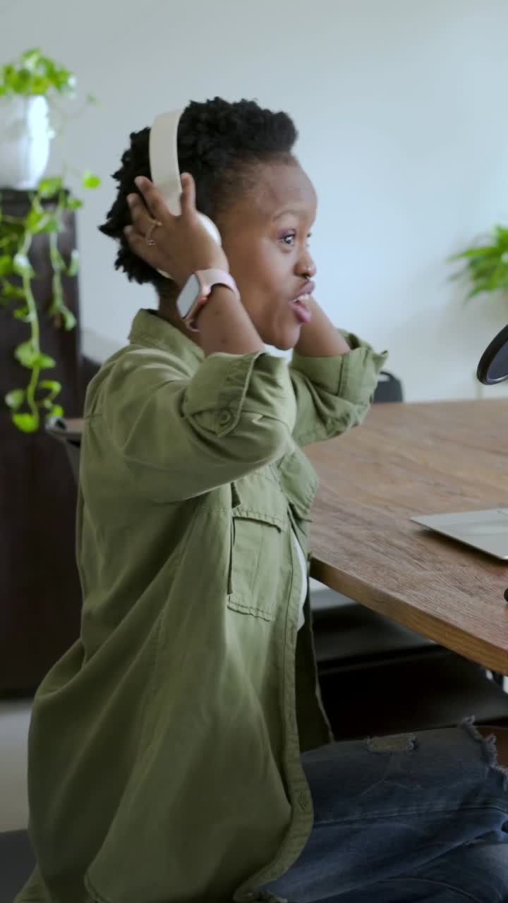Vertical video: Leaning host white headset green top speaking to mic at home podcasting with laptop