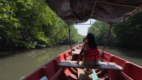 a woman in a life jacket sits in a red boat, capturing the mangrove forest's beauty - pov