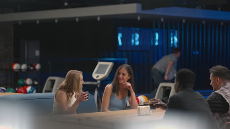 A-Caucasian-brunette-man-knocks-out-a-strike-in-a-bowling-alley-and-runs-up-to-her-friends-to-rejoice-together-and-give-five-Together-with-friends-to-celebrate-the-victory