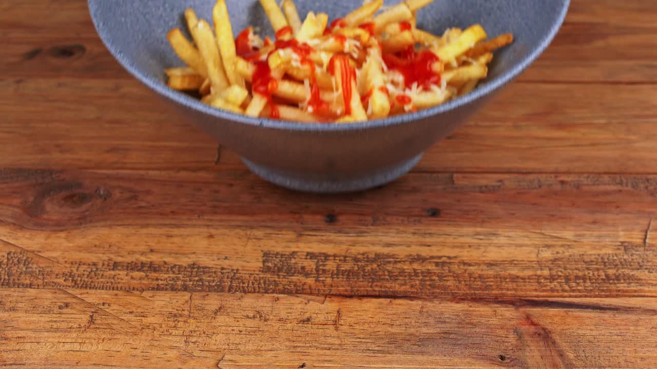Close up of grated cheese French fries smothered in catsup sauce removed from the table