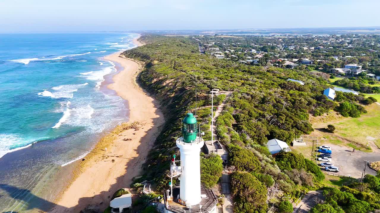 Drone footage captures Point Lonsdale's lighthouse and coastline under bright daylight, showcasing vibrant ocean hues and lush greenery