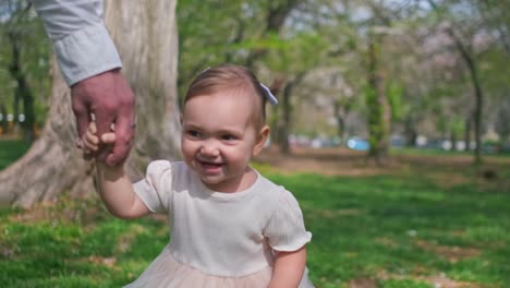 una niña caminando lentamente a través de un parque afuera mientras sostiene la mano de su padre y ríe