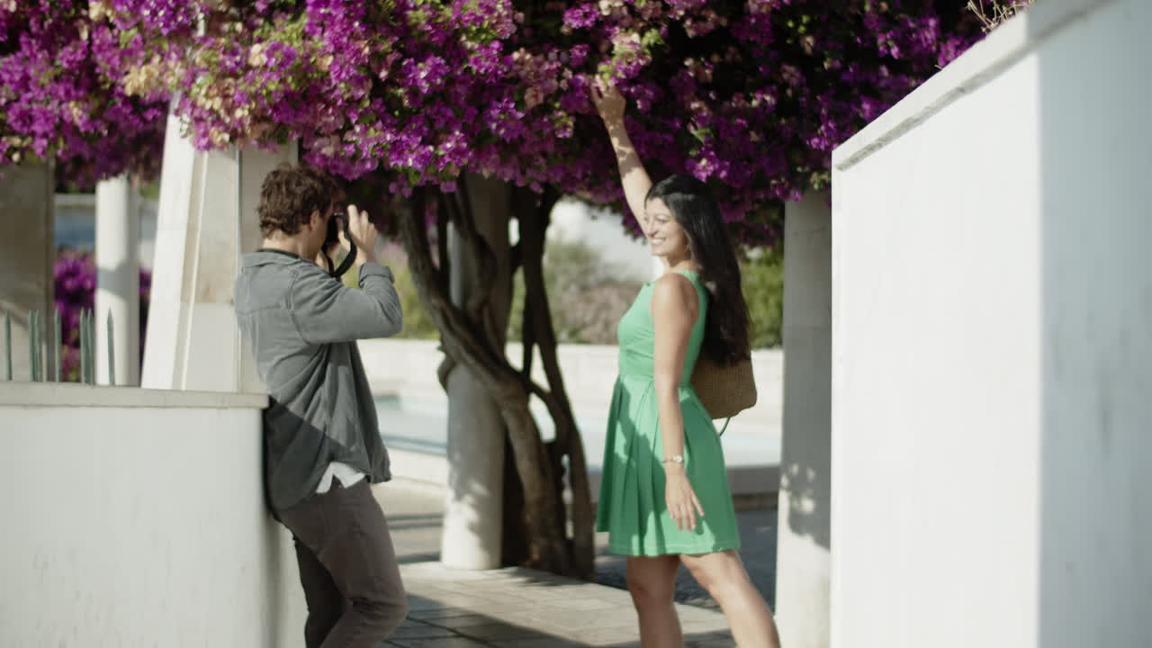 una joven pareja feliz tomando fotos bajo un árbol de buganvilla.
