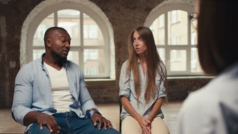 a guy with black skin in a blue shirt talks with a blonde girl in a blue shirt and a psychologist. international couple at an