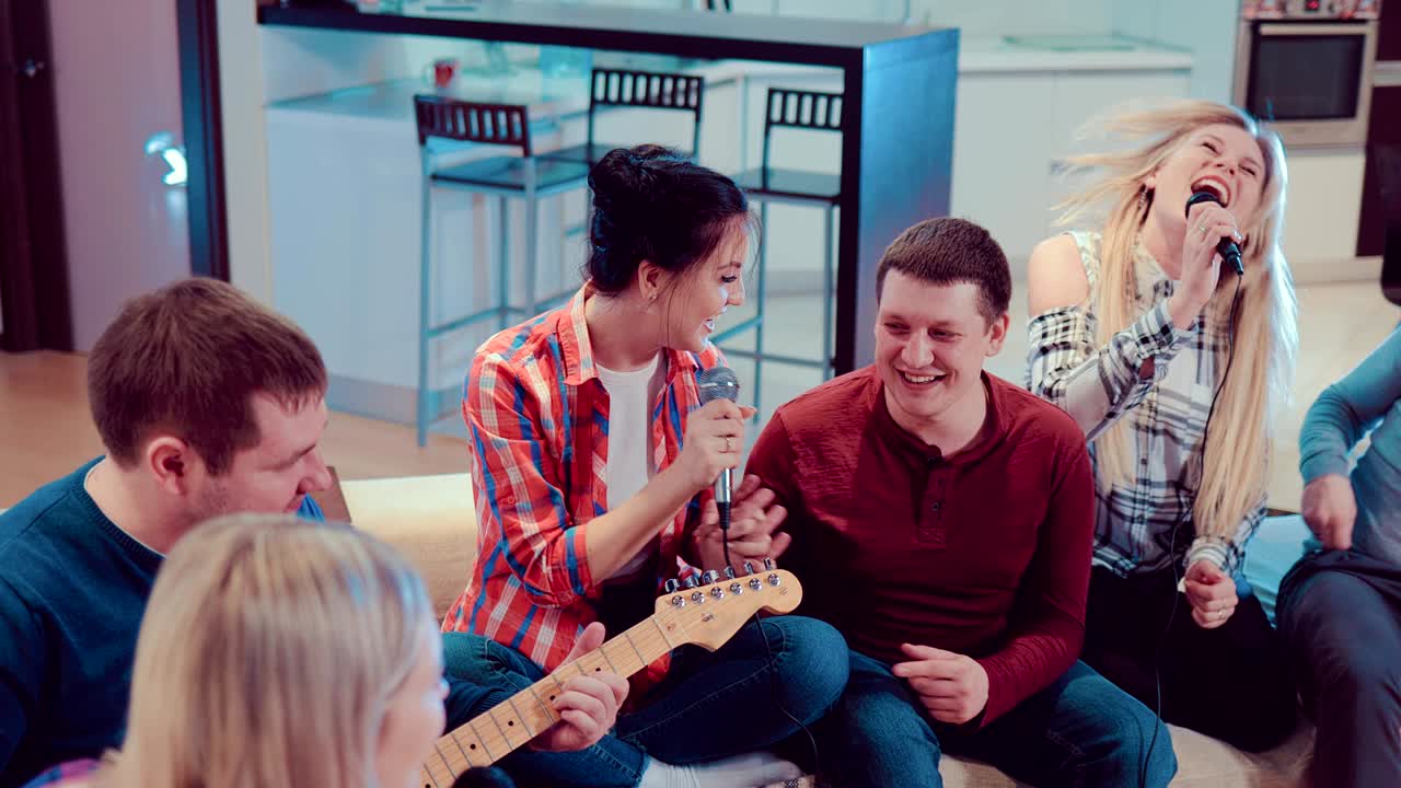 소파에 앉아 기타를 연주하고 노래를 부르는 젊은 스터 친구 그룹.