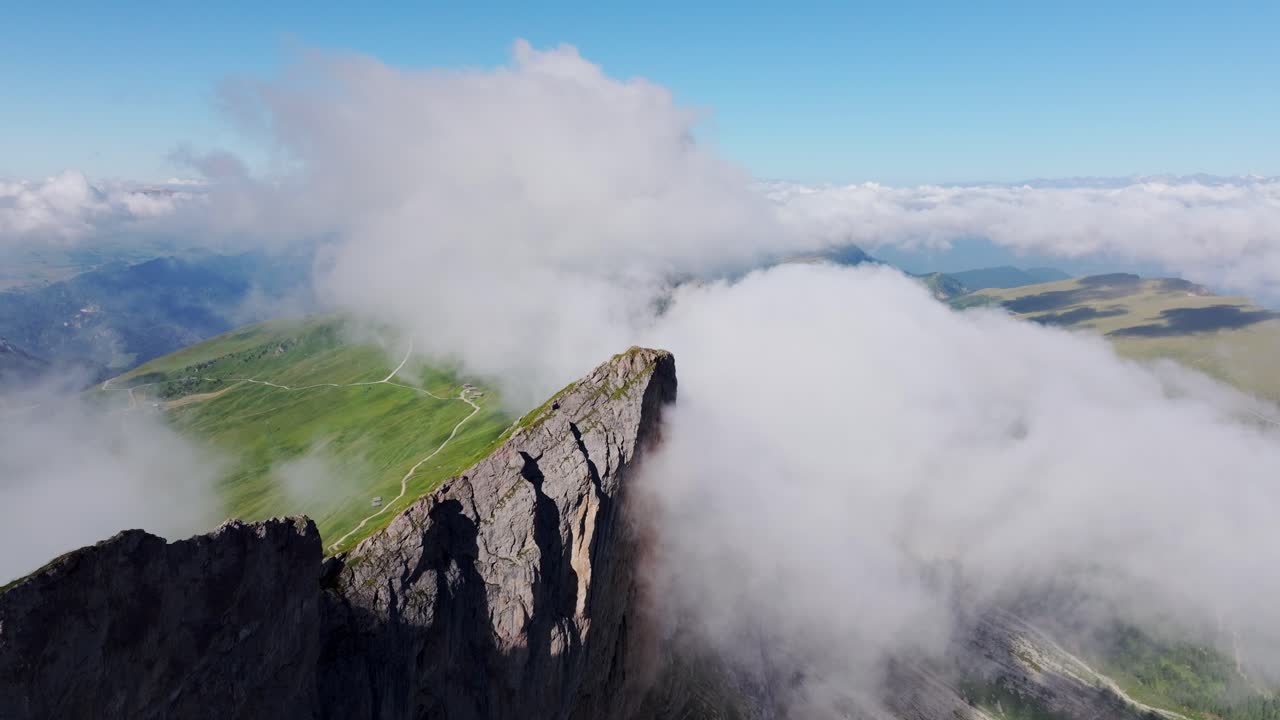 Drone moves forward towards a rugged cliff shrouded in misty summer clouds