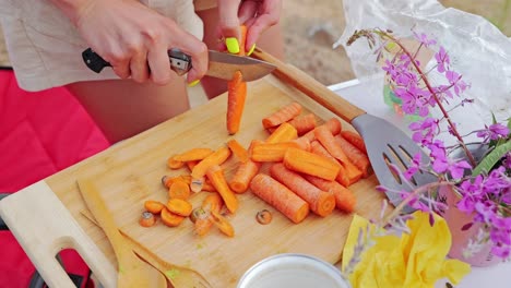 slow motion view of woman peeling carrots by hand with knife at rustic camp